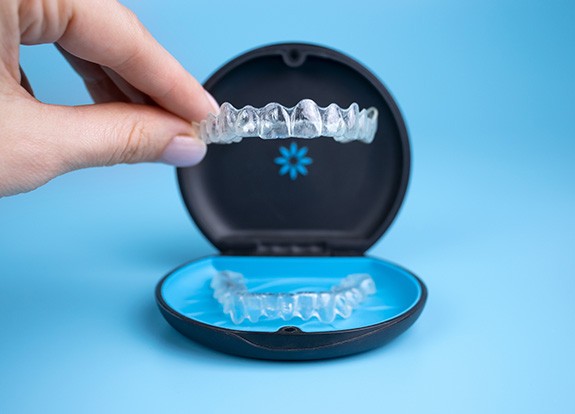 Fingers grasping Invisalign tray from its carrier case
