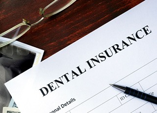 Top of dental insurance form with pen, glasses, money, and X-rays