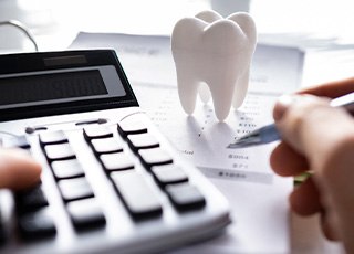 Hand touching calculator and holding pen with large model tooth on pile of invoices