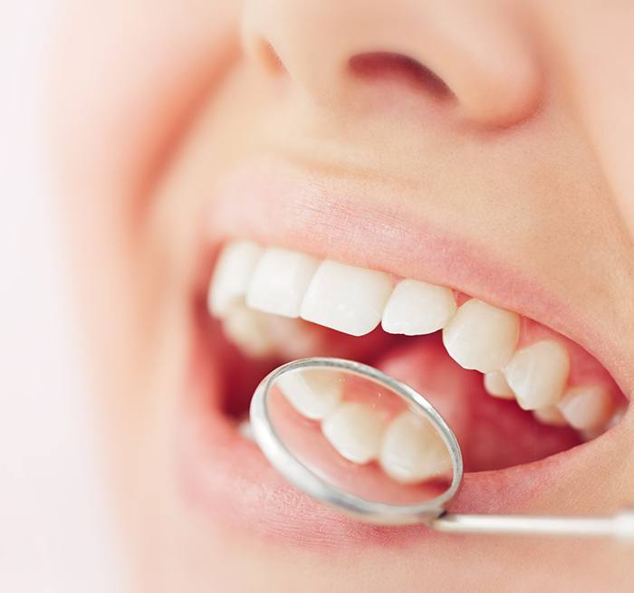 Woman in denim shirt pointing to her smile with two hands with blue background