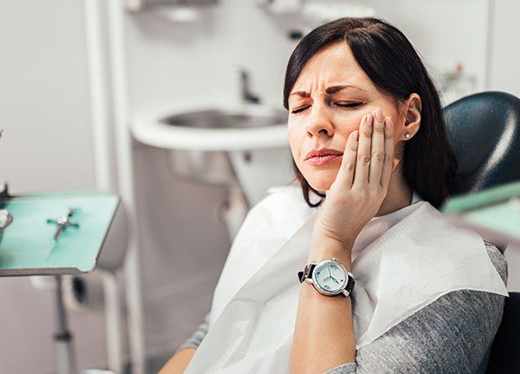 Woman in need of emergency dentistry holding cheek in pain