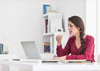 woman sitting at a desk and chewing on a pencil 