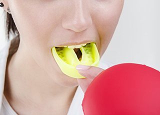 person putting a yellow mouthguard into their mouth 