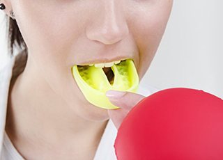 person putting a yellow mouthguard into their mouth