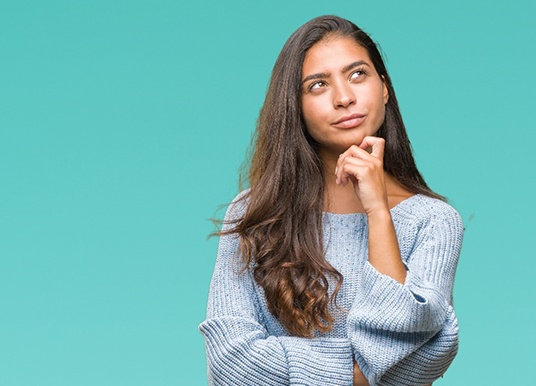 Woman on teal background wondering about dental implants in Grand Prairie 