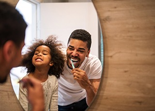 Father and daughter smiling while brushing teeth in bathroom