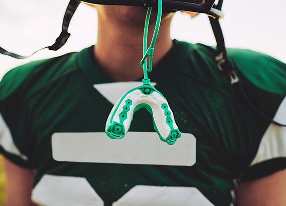 Football player with green athletic mouthguard attached to helmet