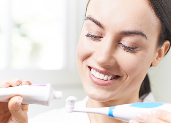 Smiling woman putting toothpaste on toothbrush