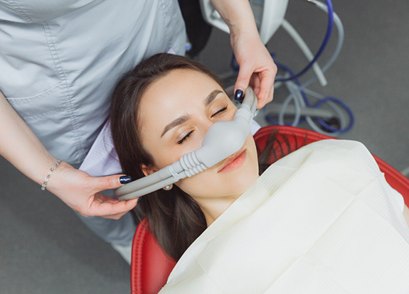 A dentist placing an inhalation sedative mask on a woman