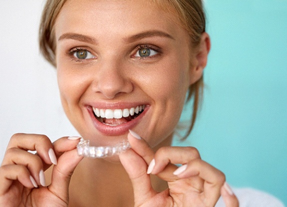 Woman smiling while holding take-home teeth whitening tray