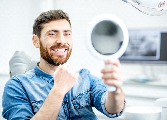 Man smiling while looking in dental mirror