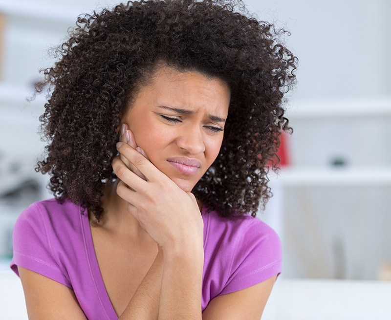 Woman in need of tooth extraction holding jaw in pain