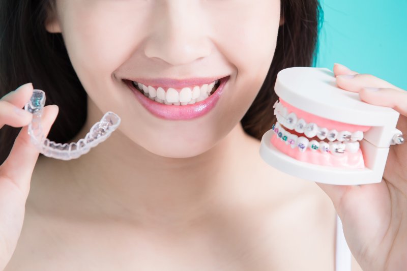 Patient holding up model of braces and Invisalign aligner