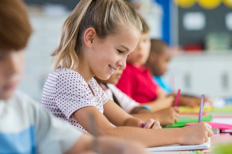 A young, smiling girl writing in her school notebook