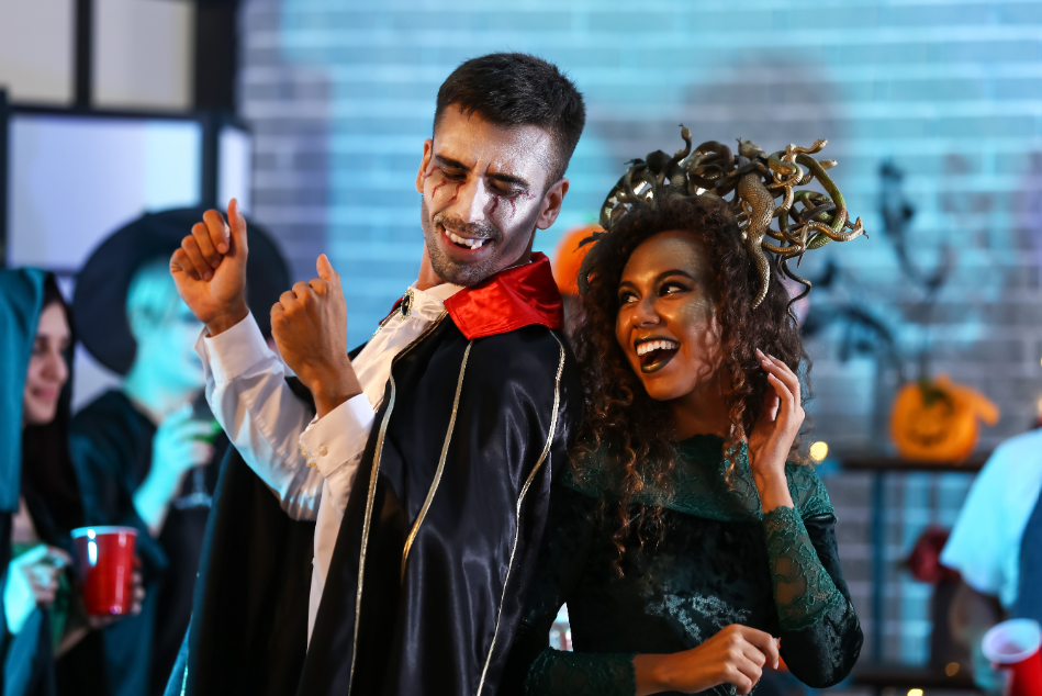 Couple at Halloween party dressed as a vampire and medusa, dancing and smiling with fangs